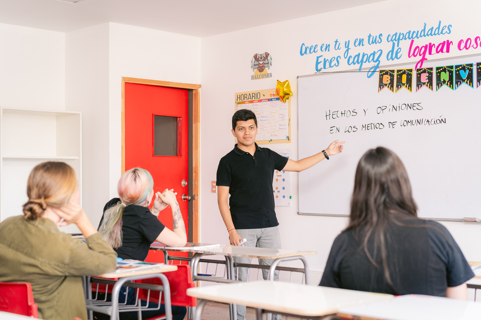Profesor en pizarra frente a estudiantes, aula con puerta roja — Elige Educar Mineduc